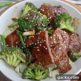 square closeup image of mongolian beef and broccoli served in a white bowl and garnished with sesame seeds.