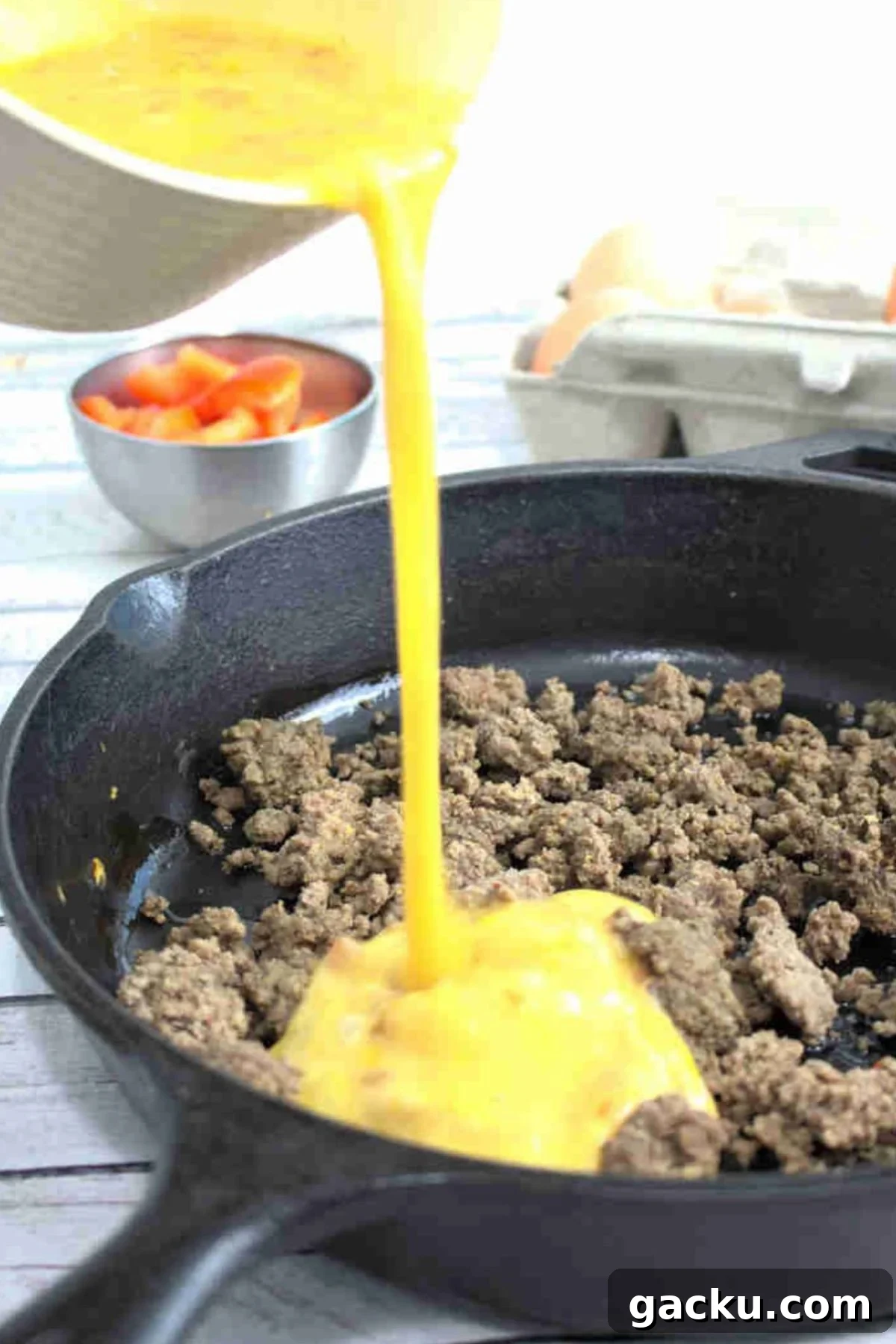 Scrambled eggs being poured into cooked ground beef in a cast iron pan.