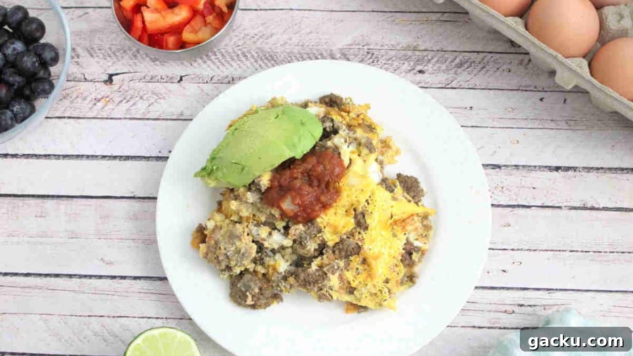 Scrambled eggs and beef on a white plate topped with salsa and avocado.