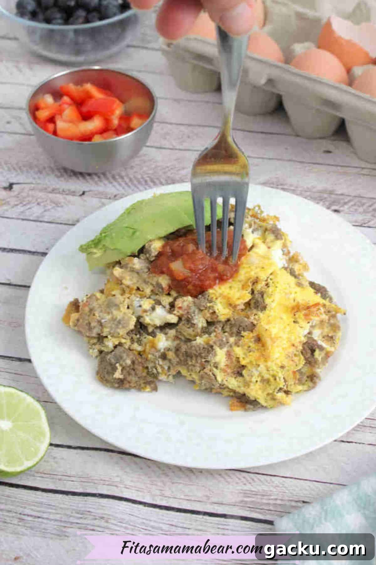 Scrambled eggs and beef on a white plate topped with salsa and avocado and a fork in the eggs.
