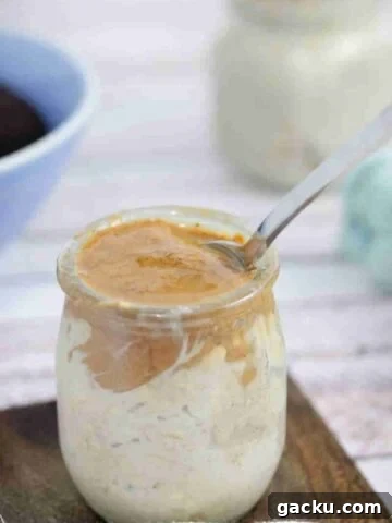 Mason jar with espresso overnight oats topped with almond butter and a spoon in it.