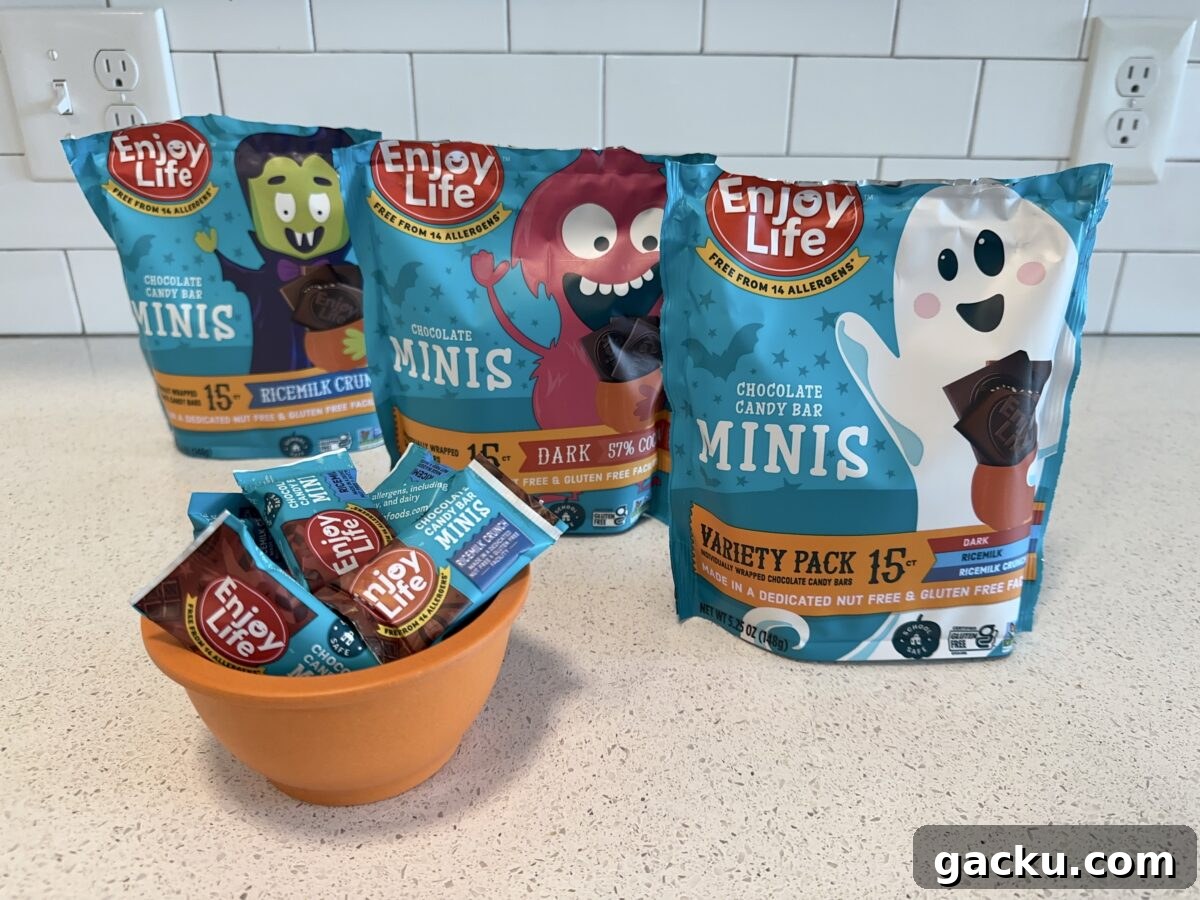 A countertop is shown with an orange bowl full of Enjoy Life brand chocolate candy bar minis, with three larger bags of the same product standing behind it.
