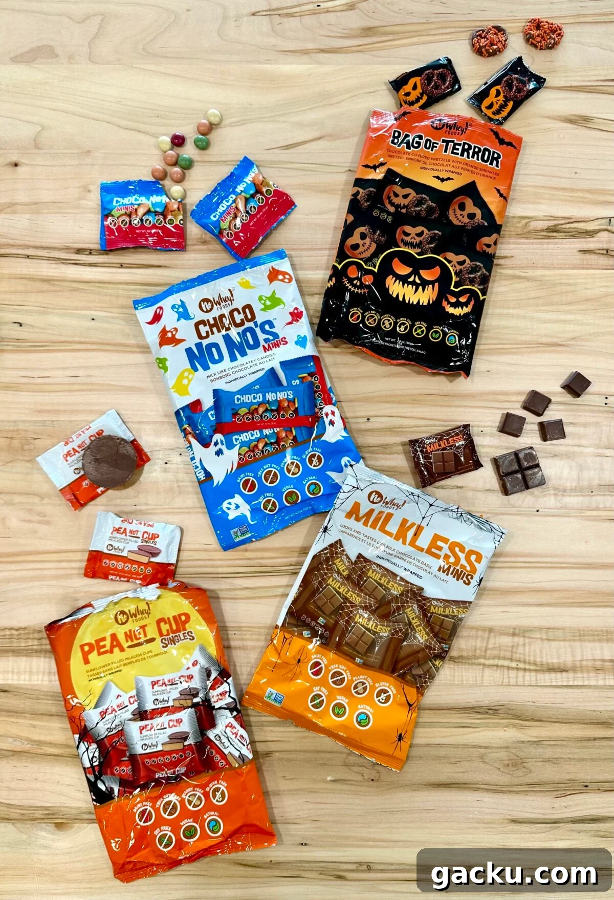 A selection of No Whey brand Halloween candy, including Choco No No's, Milkless Minis, and PeaNot Cup Singles, is scattered across a wooden surface along with a bag labeled 