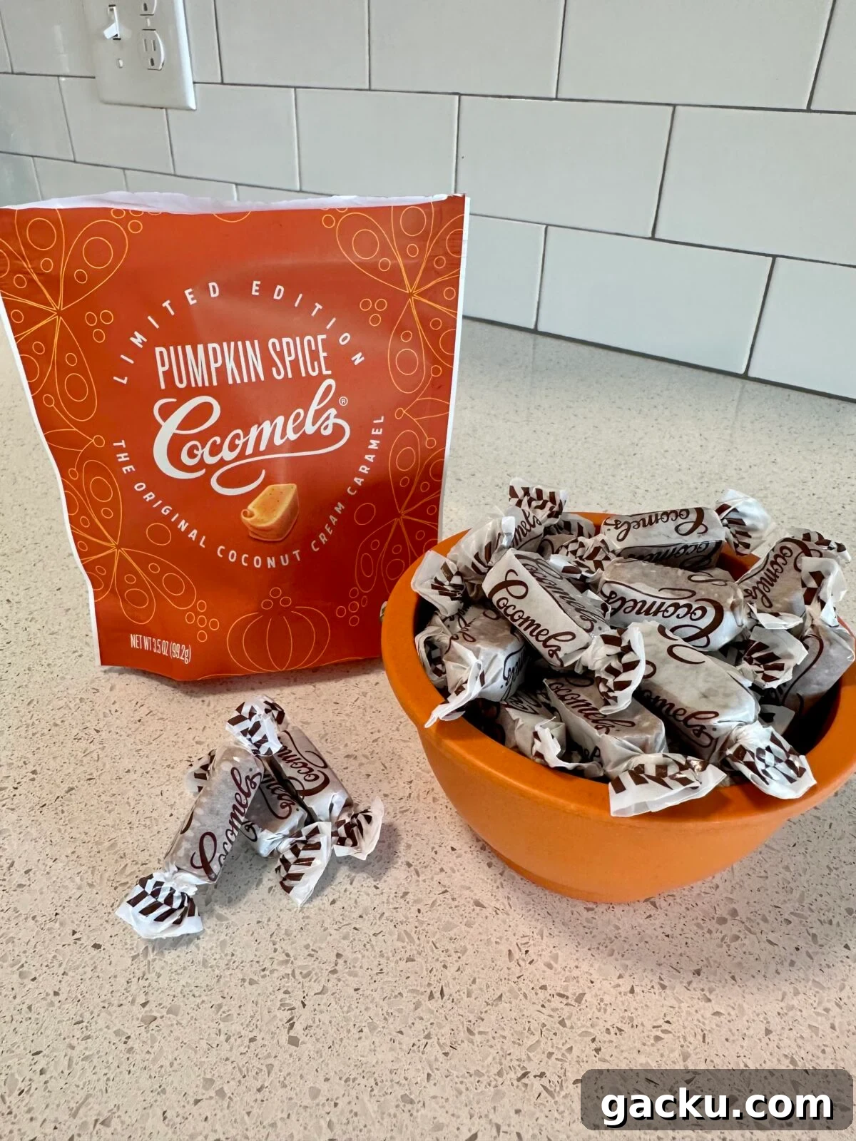 An orange bag of Limited Edition Pumpkin Spice Cocomels coconut cream caramels is on a kitchen counter next to an orange bowl overflowing with the individually wrapped candies.