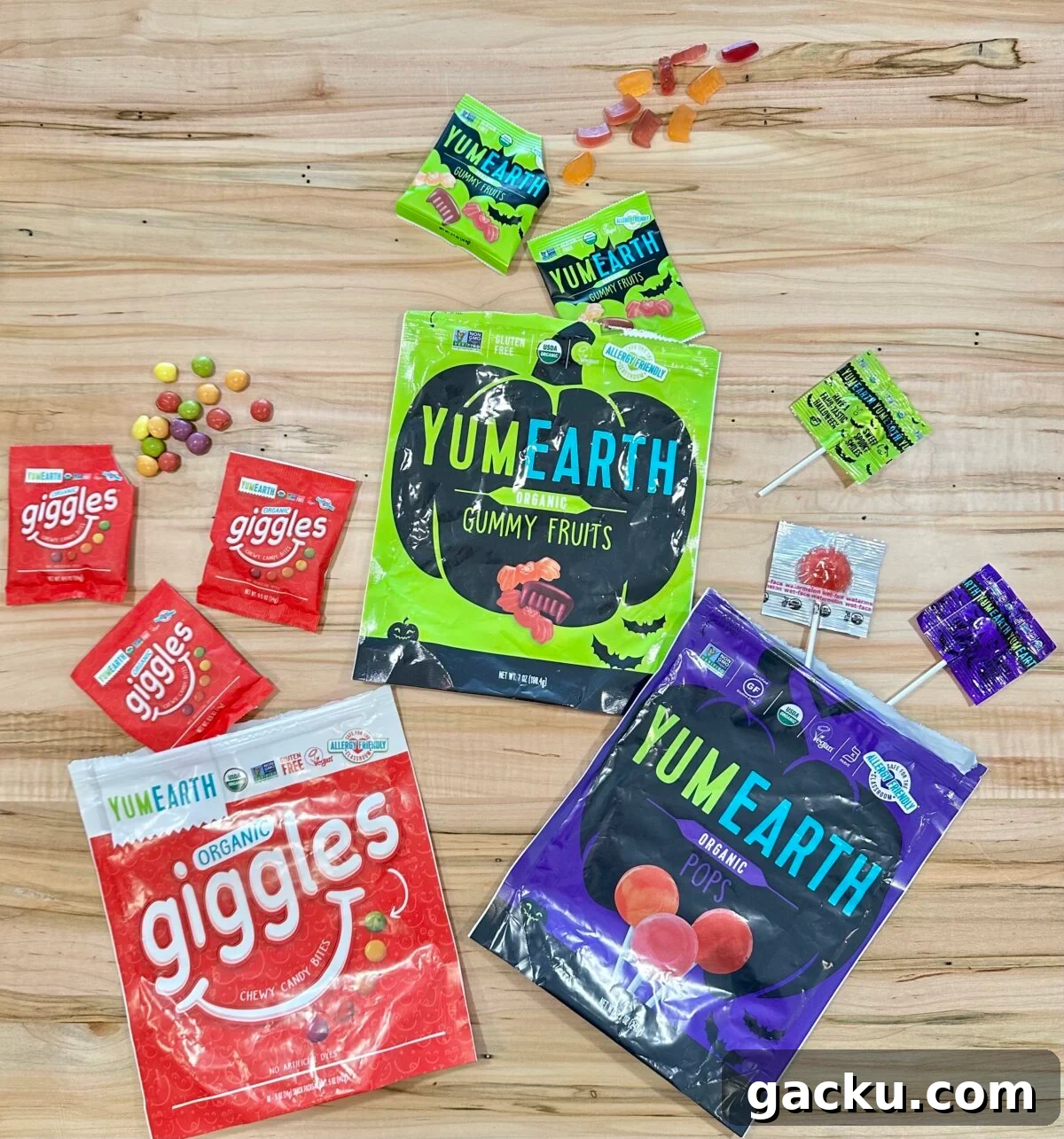 A collection of YumEarth and Giggles organic Halloween candies arranged on a light-colored wooden surface, including bags of gummy fruits, lollipops, and chewy candy bites.