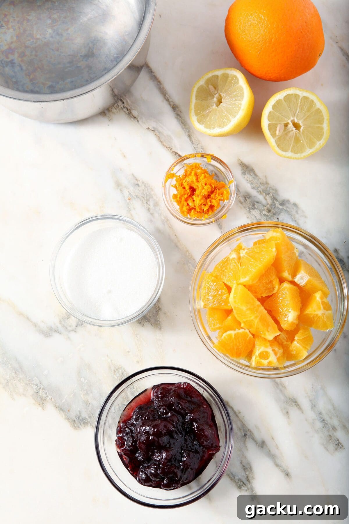 Ingredients to make cranberry compote in bowls on marble next to a saucepan