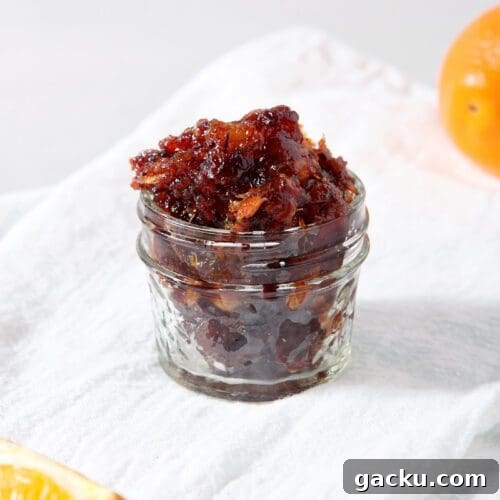 A jar of cranberry compote on a white linen towel next to orange slices