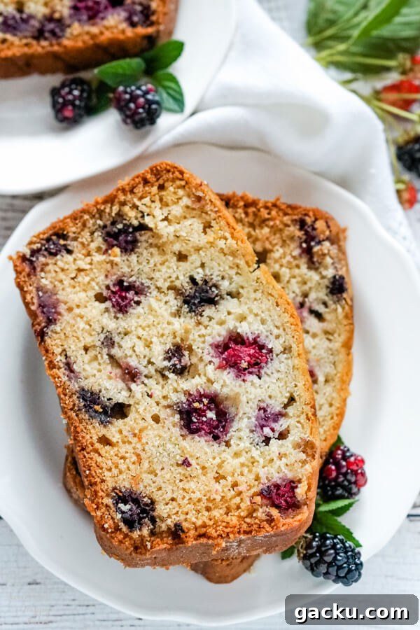 Moist Homemade Blackberry Bread Recipe for Summer Baking 5 Two slices of blackberry bread on a white plate with fresh blackberries by the side.