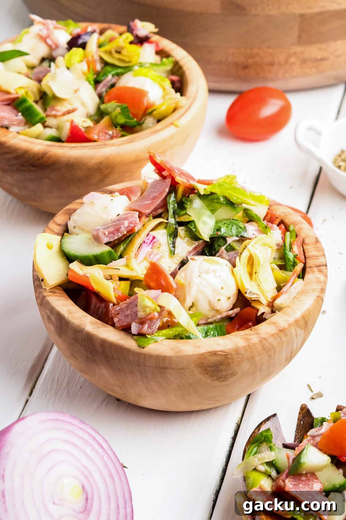 Two small wooden bowls filled with Italian antipasto salad including mozzarella, meats, lettuce, and vegetables.