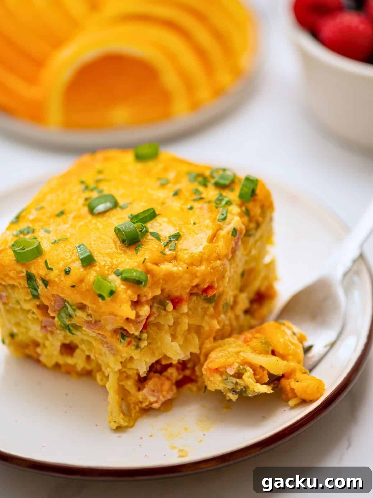 Slice of crockpot breakfast casserole with hashbrowns, ham, and cheese on plate topped with sliced green onions.
