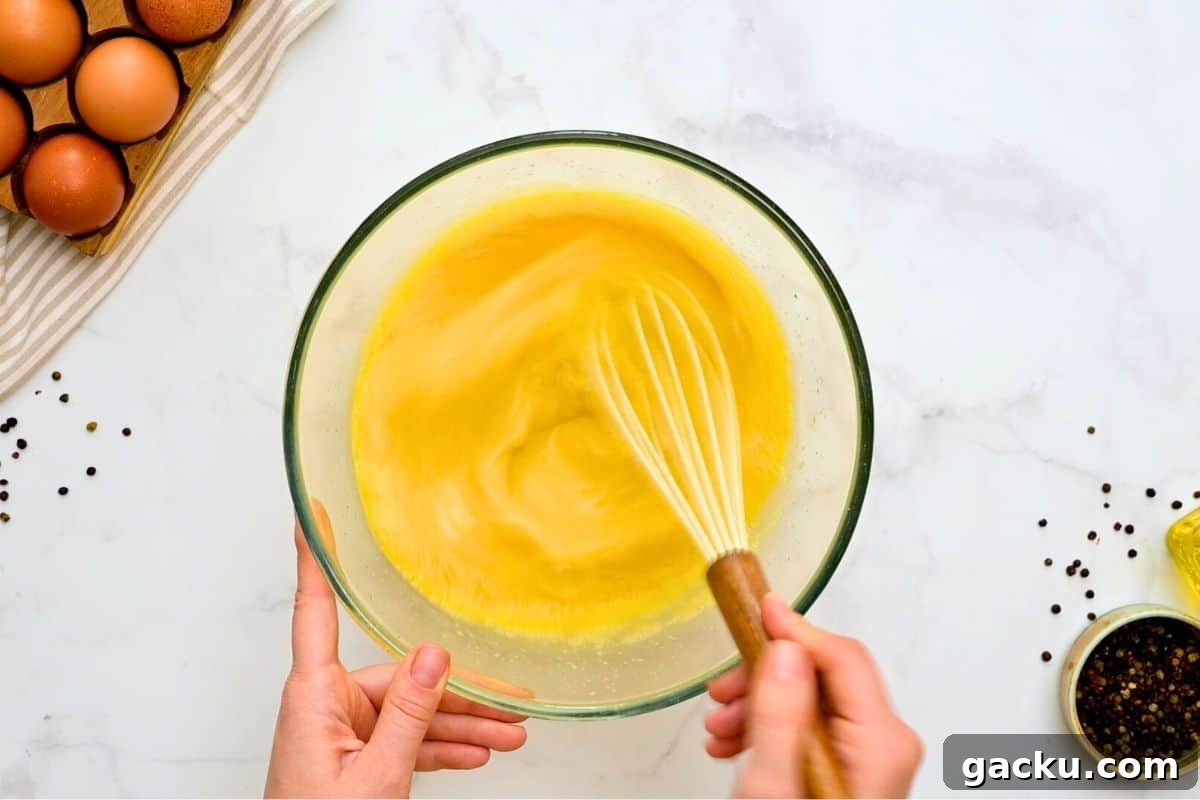 Mixing bowl with 12 eggs and milk being whisked by hand for egg casserole.
