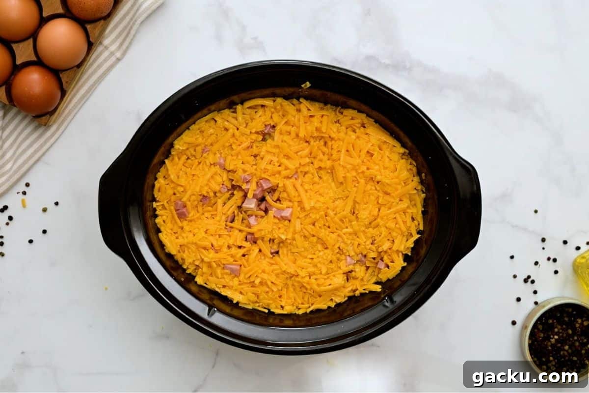 Hash browns, cheese, ham, peppers, and eggs layered in large crockpot to make crockpot breakfast casserole.
