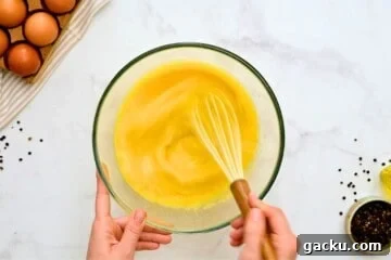 Mixing bowl with 12 eggs and milk being whisked by hand for egg casserole.