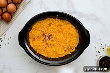 Hash browns, cheese, ham, peppers, and eggs layered in large crockpot to make crockpot breakfast casserole.