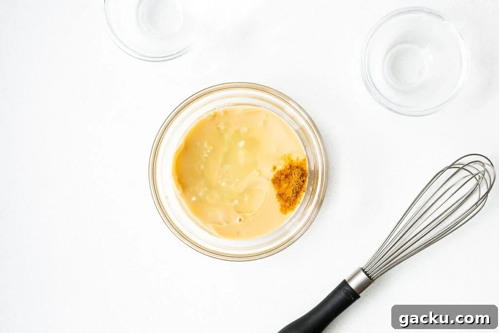 Tahini sauce ingredients in a small glass bowl next to an unused whisk.
