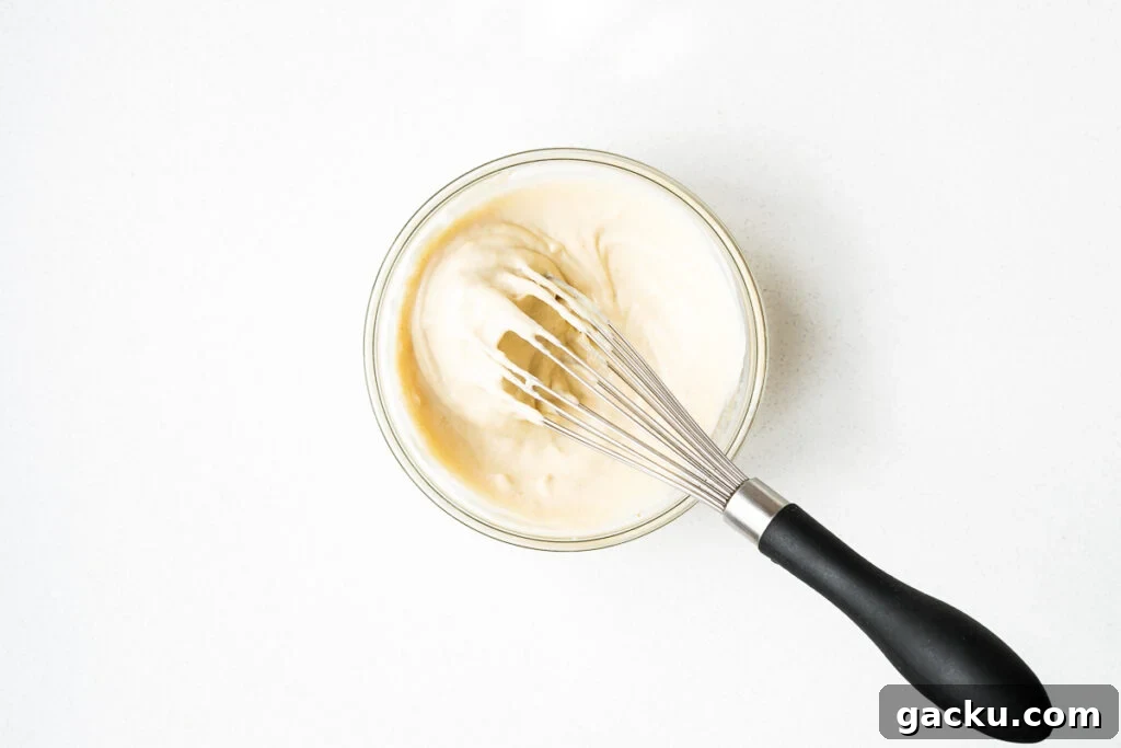 Tahini sauce for Israeli salad in a small mixing bowl with a whisk.