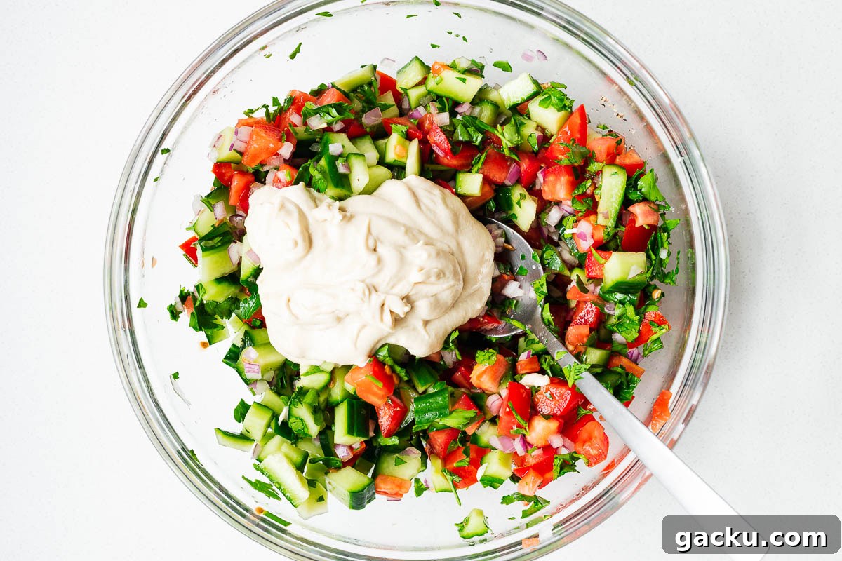Israeli chopped salad (Jerusalem salad) topped with tahini sauce in a glass bowl before mixing.