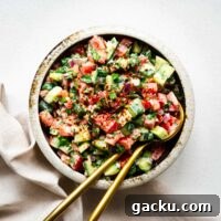Jerusalem salad (Israeli salad) with tahini sauce in a bowl with golden serving spoons viewed from above.