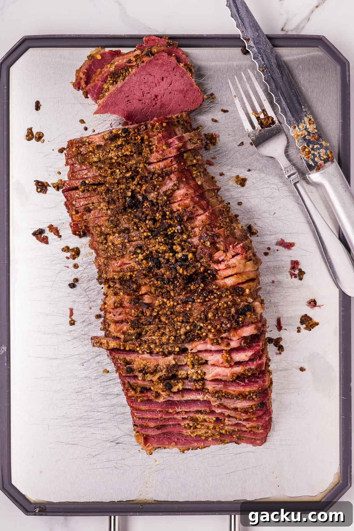 Sliced corned beef with a mustard and spice crust on a cutting board, accompanied by a knife and fork.