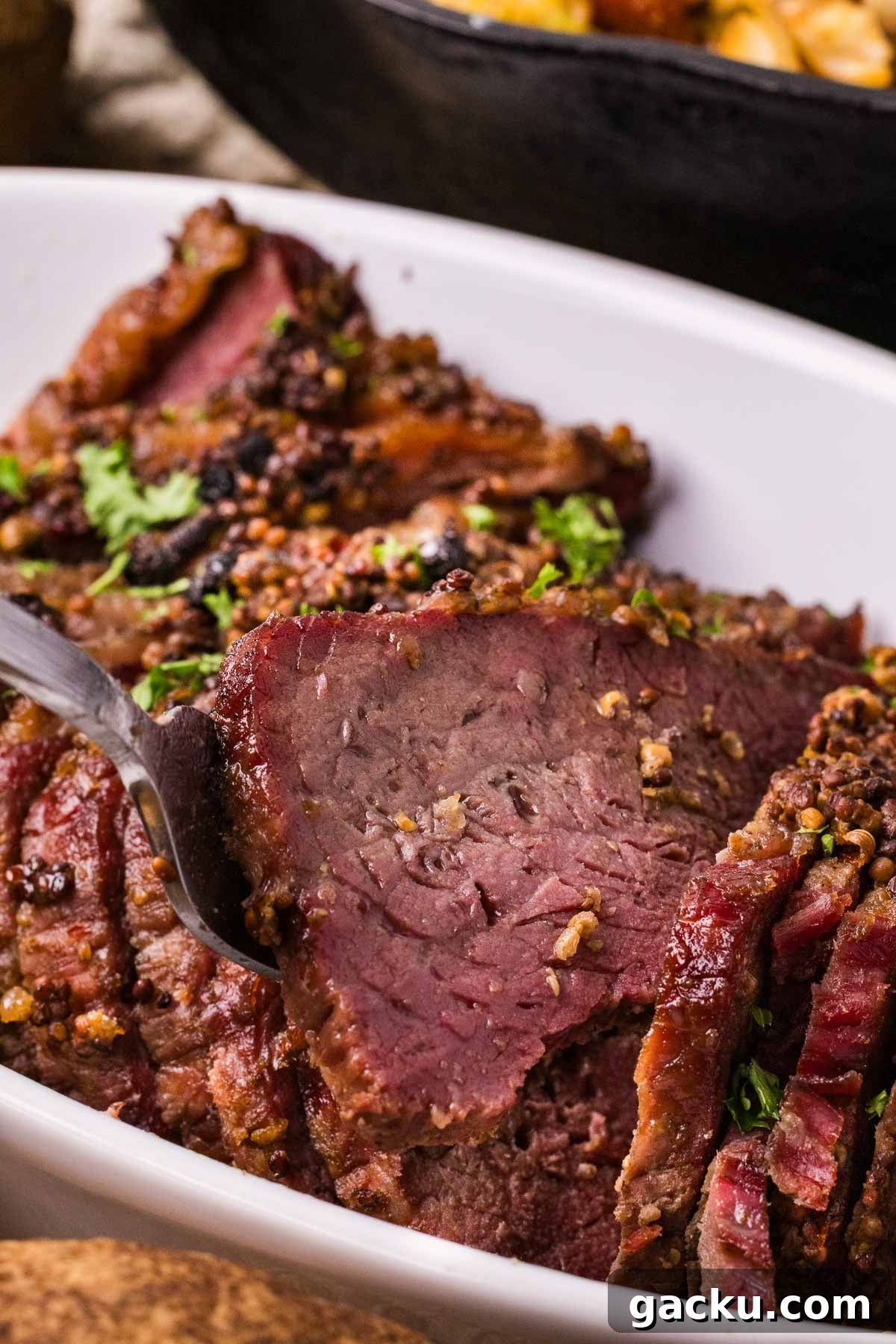 Sliced smoked and braised corned beef brisket garnished with herbs in a white dish, with a fork lifting one slice.