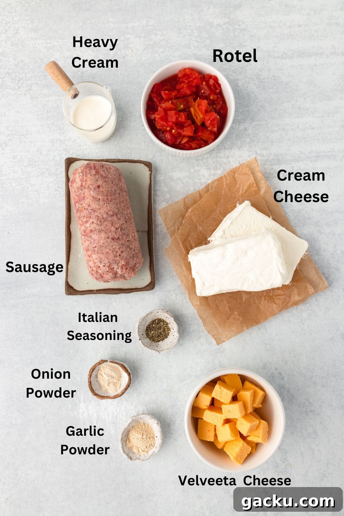Ingredients for a creamy dip include a block of raw sausage, a cup of heavy cream, a can of Rotel, cream cheese, Velveeta cheese cubes, and small bowls of Italian seasoning, onion powder, and garlic powder, arranged on a light surface.