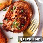 Crispy Air Fryer Pork Chops from Frozen in 20 Minutes 8 cooked frozen pork chops with chives on top on a white plate with a gold fork