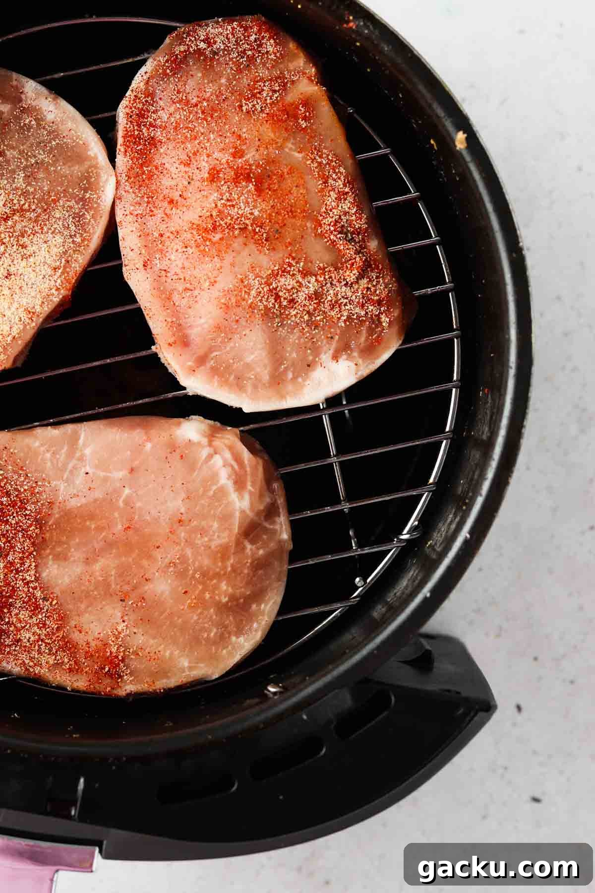 Crispy Air Fryer Pork Chops from Frozen in 20 Minutes 2 raw pork chops on a rack in the air fryer