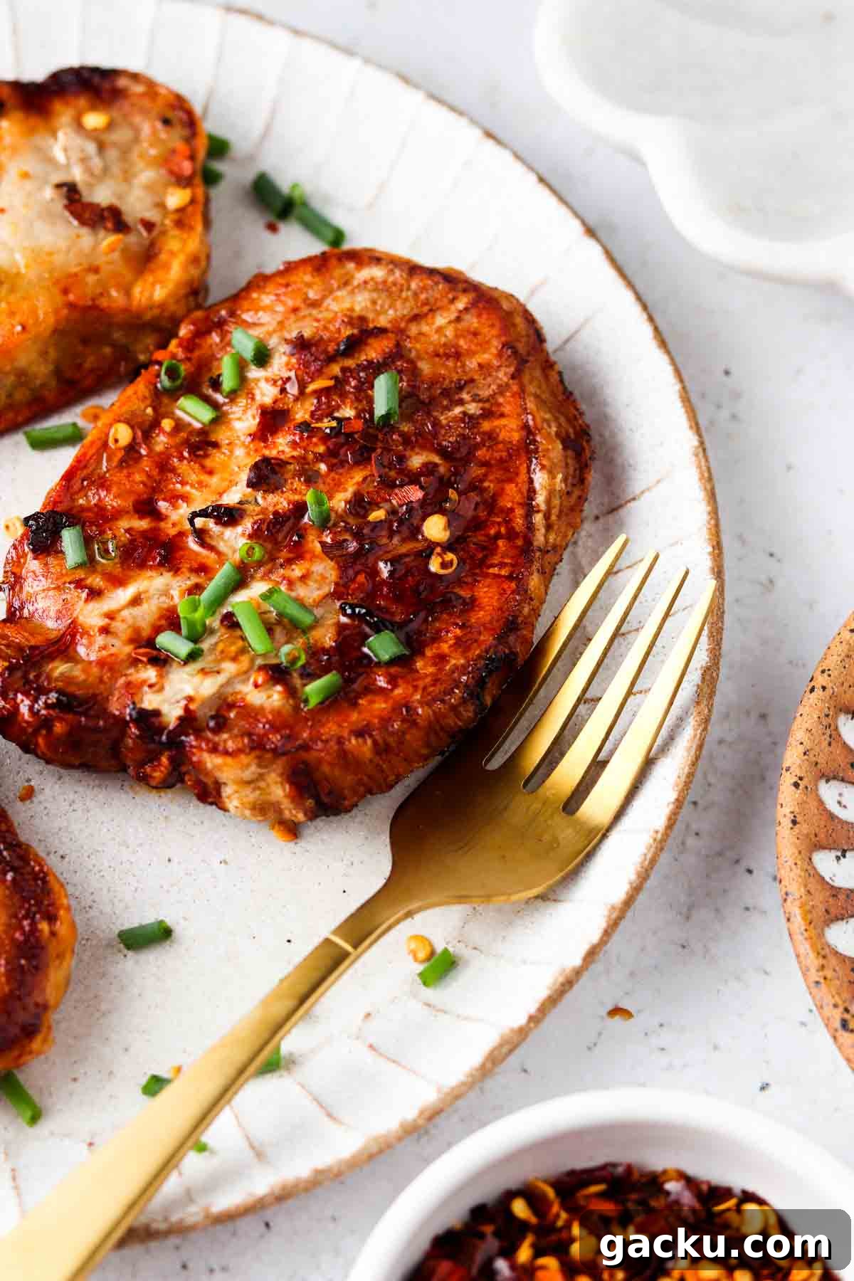 frozen pork chops air fryer 5 Cooked pork chops on a white plate with a gold fork and garnished with chives and red pepper flakes.