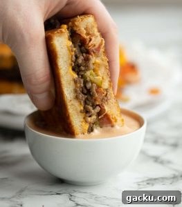 dunking halves a grilled cheese into small pot of burger sauce